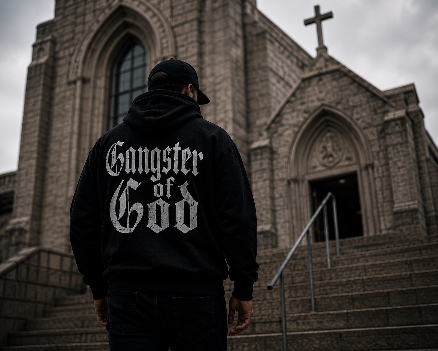 A man wearing a Gangster of God hoodie standing outside a stone church