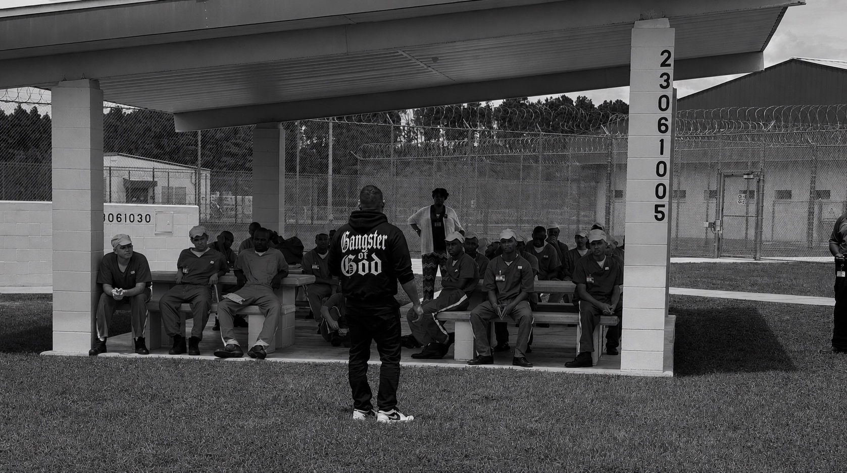 A man in a Gangster of God hoodie speaking with men gathered in a prison recreation yard